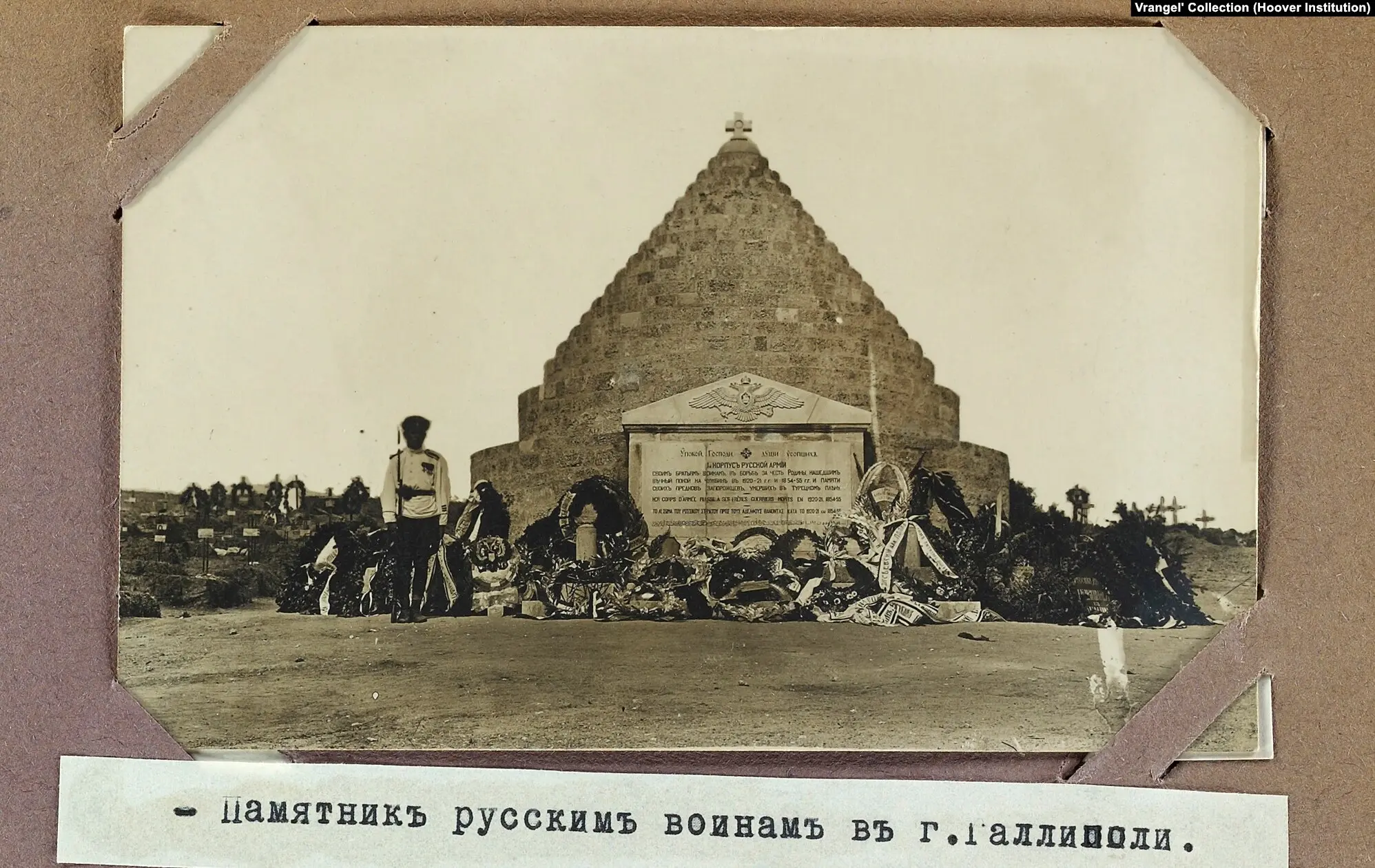 A sepia-toned photo depicts a pyramid-shaped memorial with a cross on top, surrounded by wreaths. A solitary figure stands nearby.